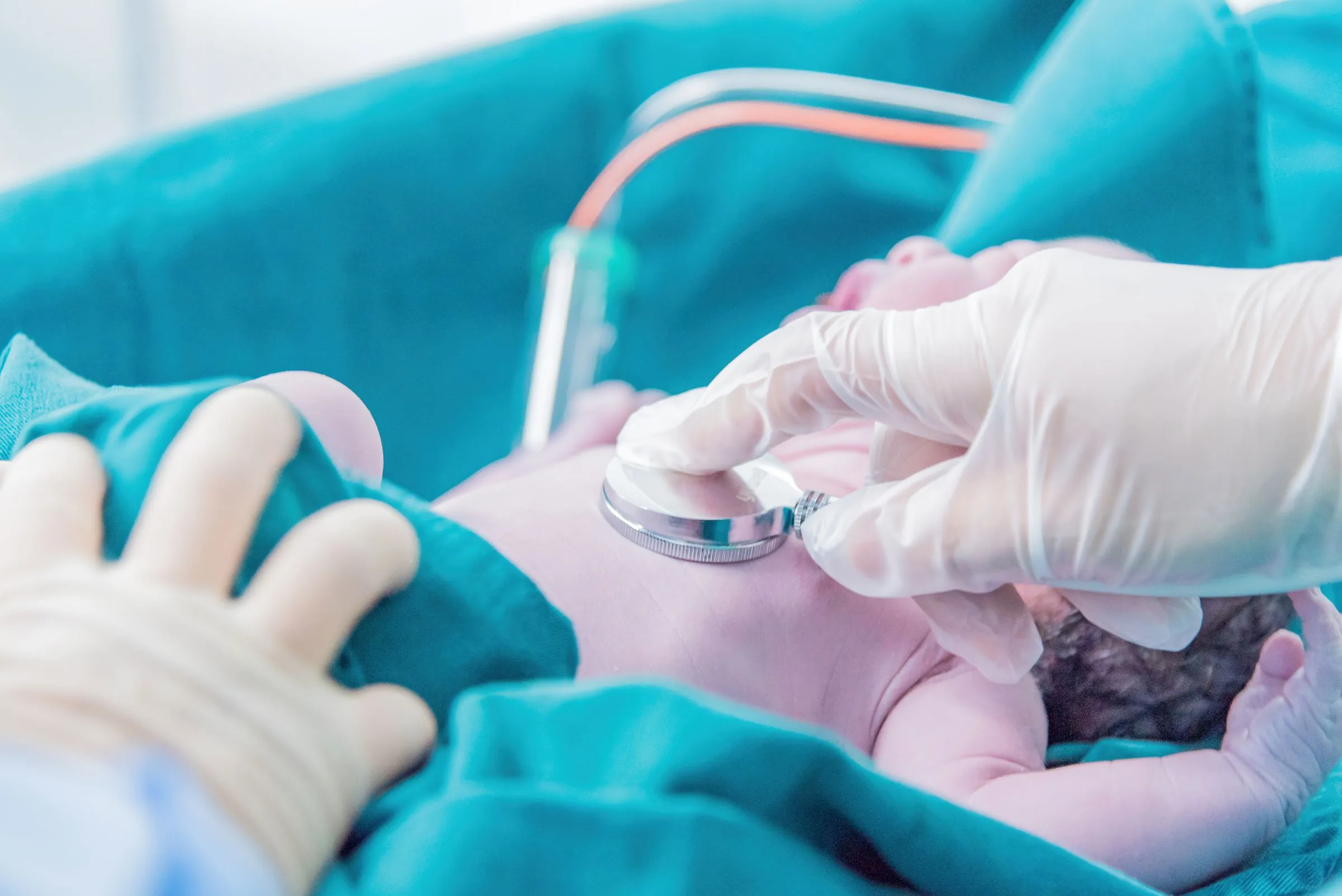 A gloved clinician listening to a newborn's chest with a stethoscope