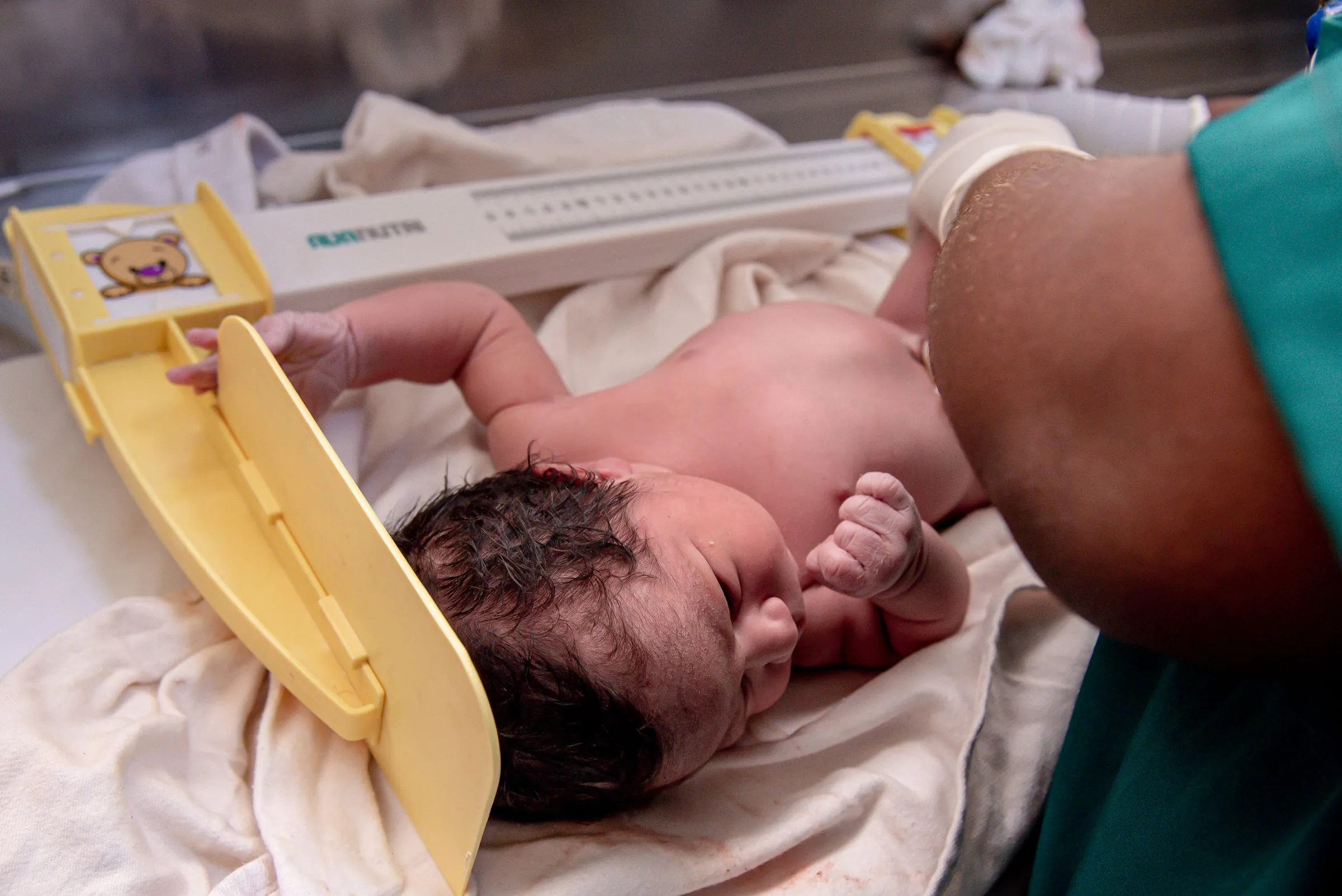 A newborn being measured on a length board by a healthcare worker