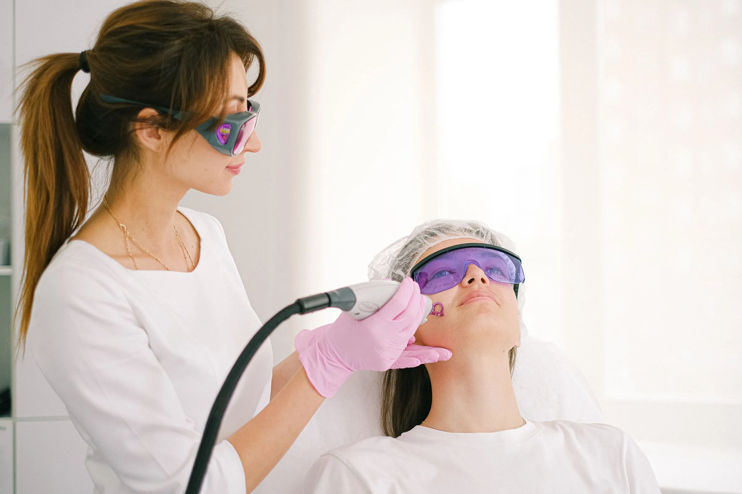A clinician performing a laser facial treatment on a patient wearing eye protection