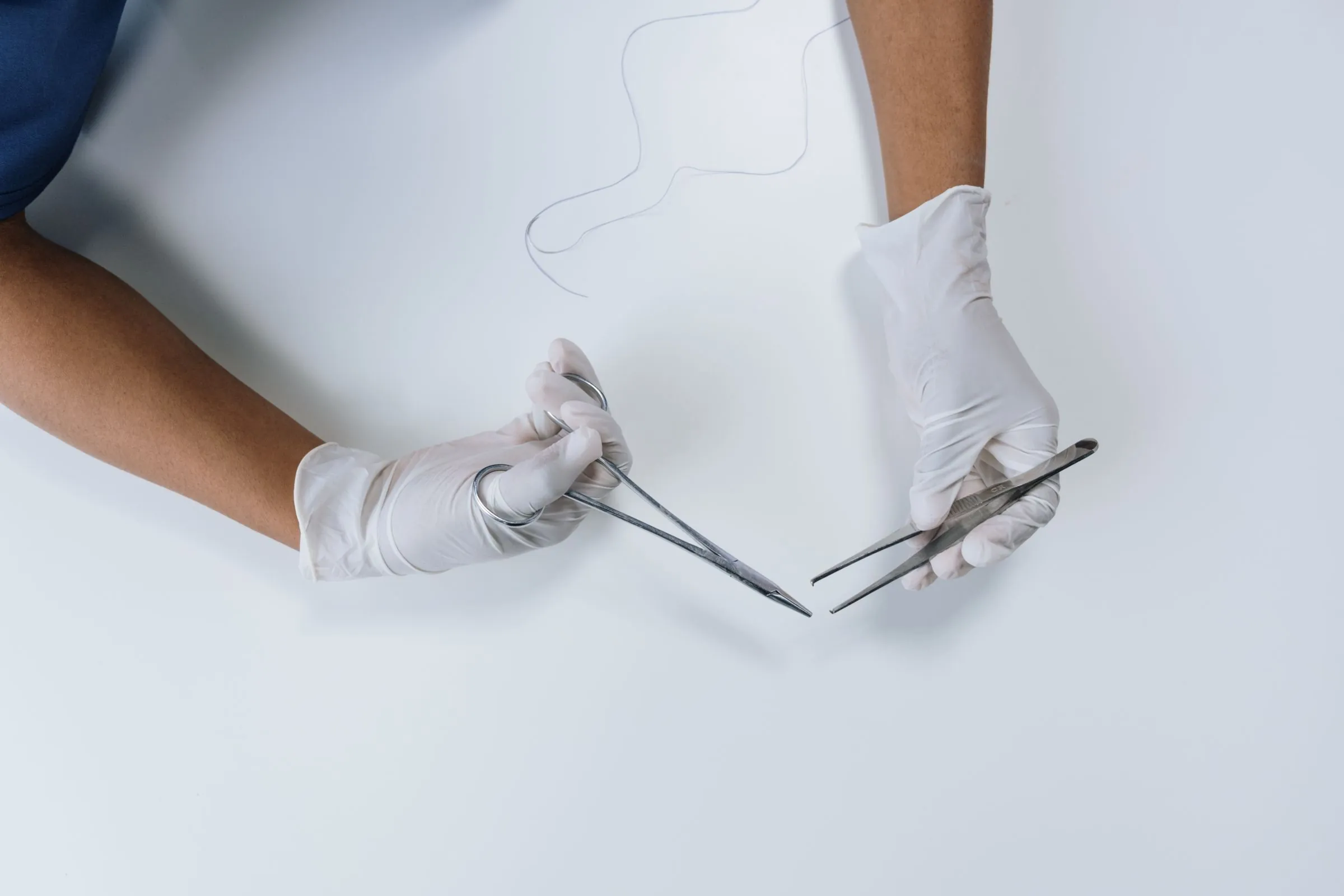 Gloved hands holding surgical forceps and scissors over a sterile field